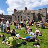 People relaxing on a lawn in front of a restored castle.