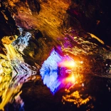 Underground slate cavern colourfully lit and reflecting in the water.