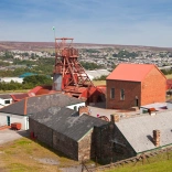 Colliery buildings and a pit head overlooking a town in the South Wales valleys.