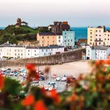 Looking down toward a harbour with boats on the sand and colourful houses and the sea in the background.