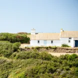 A walker on a coastal path leading to a white cottage.