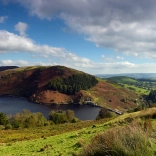 Landscape image of a reservoir, surrounded by a mountain and trees.