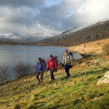 Three walkers taking a walk along the Llynnau Mymbyr lake in Snowdonia.
