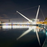 Night time view of the river with reflective white lights from the bridge and buildings on the right of the image