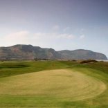 The green on a golf course with views of the coastline and cliffs beyond.