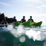 Three kayakers on the ocean with a rocky cove backdrop.
