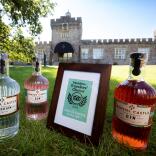 Bottles of gin and a framed award on a lawn outside a distillery.