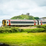 A train travelling alongside the coast and a castle on a hill.