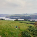 Walkers on a hill overlooking a reservoir.