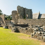 The ruins of an abbey with a church in the background.
