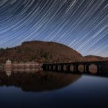 Star trails in the night sky above a reservoir.