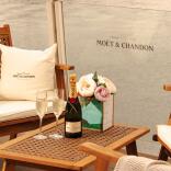 A bottle of champagne on a table with chairs on a terrace.