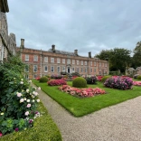 A grand house with beautiful flowers and round shrubbery in the forecourt.
