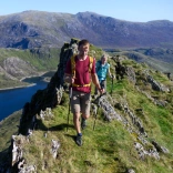 A couple walking on the top of a ridge with a lake below.