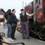A couple talking to the driver next to a steam train.