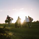 Golfers walking to the next tee on a golf course at sunrise.