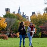 Two ladies walking through a park in the autumn with a castle in the background.