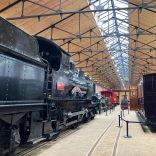 An engine shed filled with steam trains and carriages.