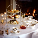 A table set up for afternoon tea with champagne next to a roaring fire.