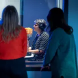 Group of people on a tour, looking through a glass screen at a presenter at work.