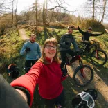 Group of people with their bikes in a bike park smiling at the camera.