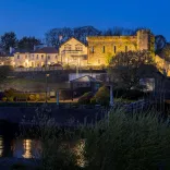 External shot of a castle hotel lit up at night, with a river running beside it.