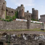 A train coming out of a turret on a castle wall with the castle beyond.