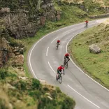 Cyclists on a road against a mountainous landscape with a Welsh dragon on the wall.