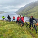 Group of cyclists surrounded by a lake and mountains.