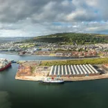 Aerial shot of a cruise shop docked at a port, witgh green mountains beyond.