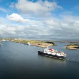 A cruise ship heading toward a port With mountains and the shoreline in the background.