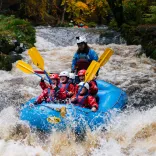 Group of people on a raft heading down rapids on a river.