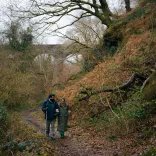 A couple walking along a forest footpath with a viaduct in the background.