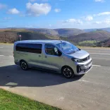 Minibus parked on an open road with a backdrop of spectacular mountains.