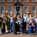 A group of people outside an grand estate holding visitor attraction leaflets.