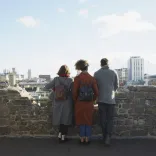 Group of people on a castle turret looking out towards the city.