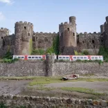 A train passing a castle next to the shoreline.