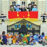 Knitted scene of the Royal Family on a balcony waving to crowds below.