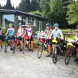 A group of cyclists outside a wooden lodge surrounded by trees. 