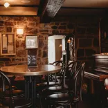 Tables, chairs and a piano in a stone walled lounge area of a hotel.
