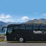 A coach parked up with views of mountains and a lake beyond.