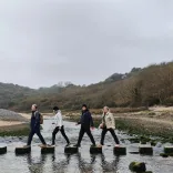Group of people walking on stepping stones over a river.
