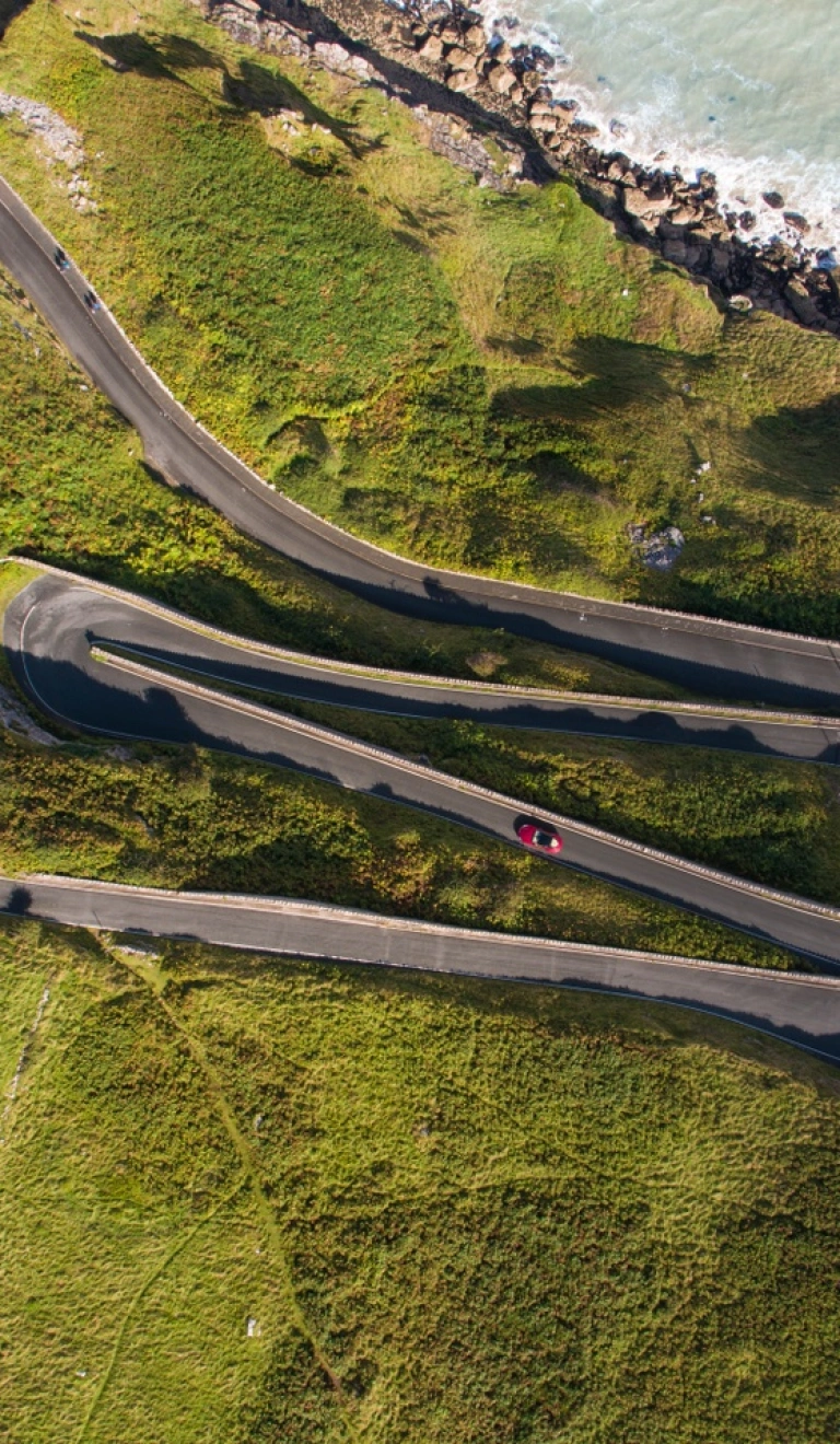 A car driving a zig zag road on a headland by the coast.