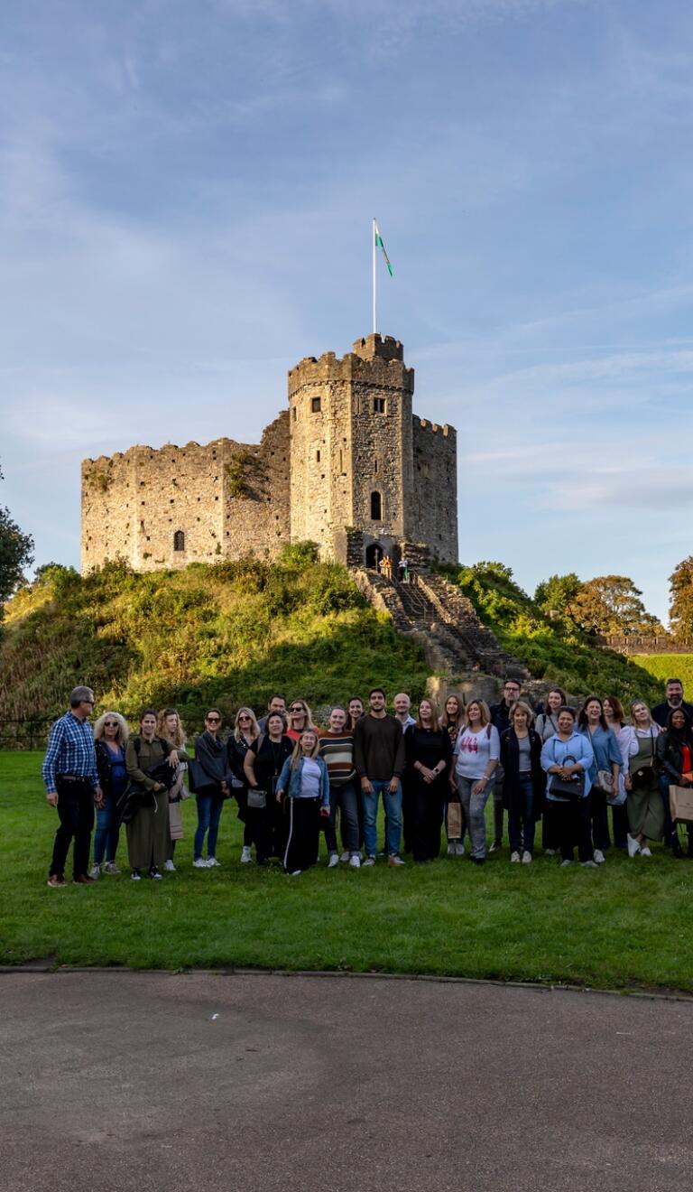Group of people standing at the foot of a castle smiling at the camera.