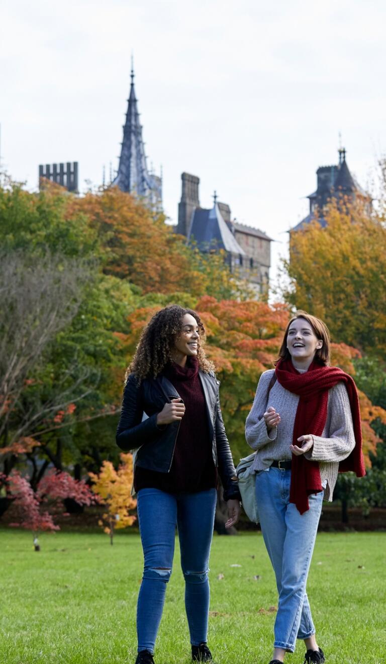 Two ladies walking through a park in the autumn with a castle in the background.