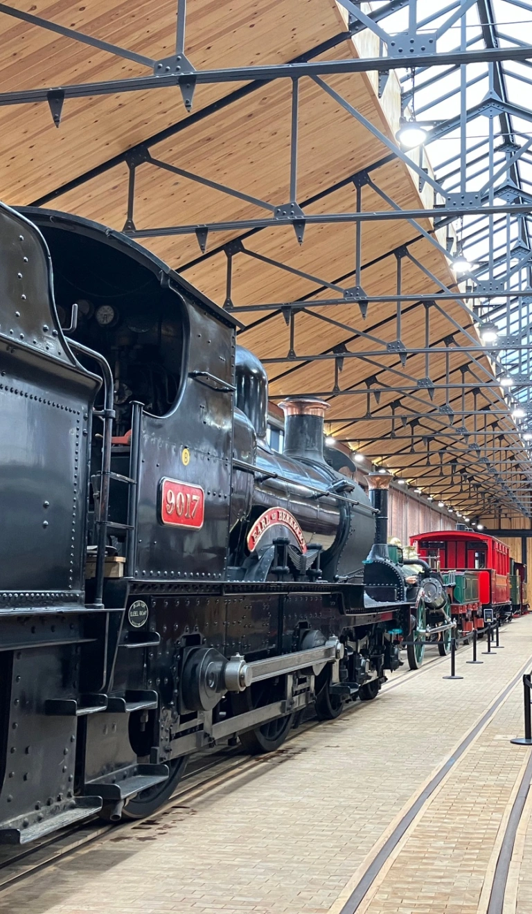 An engine shed filled with steam trains and carriages.