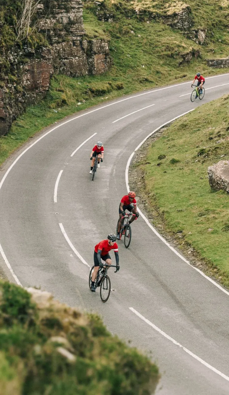 Cyclists on a road against a mountainous landscape with a Welsh dragon on the wall.