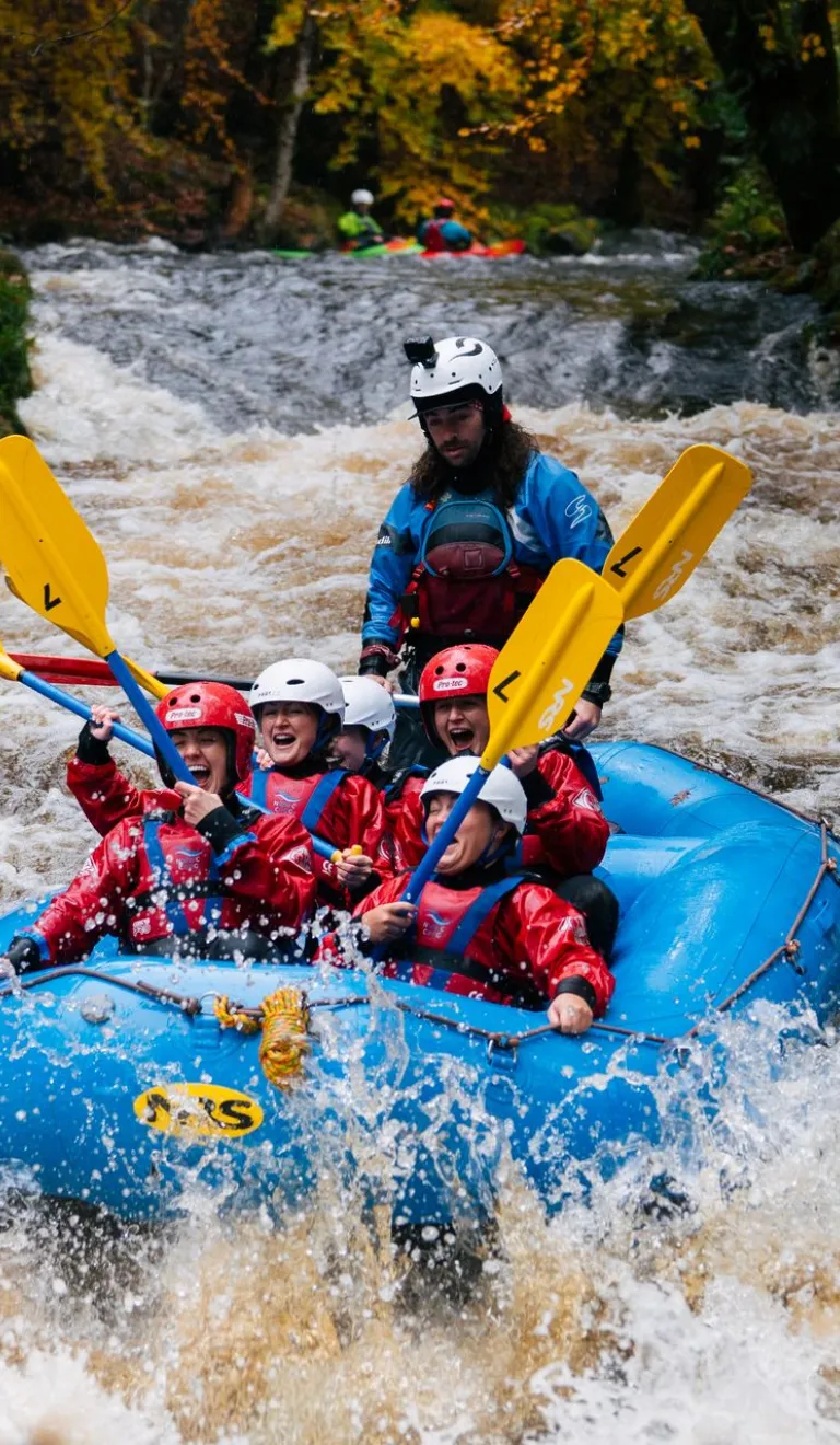 Group of people on a raft heading down rapids on a river.