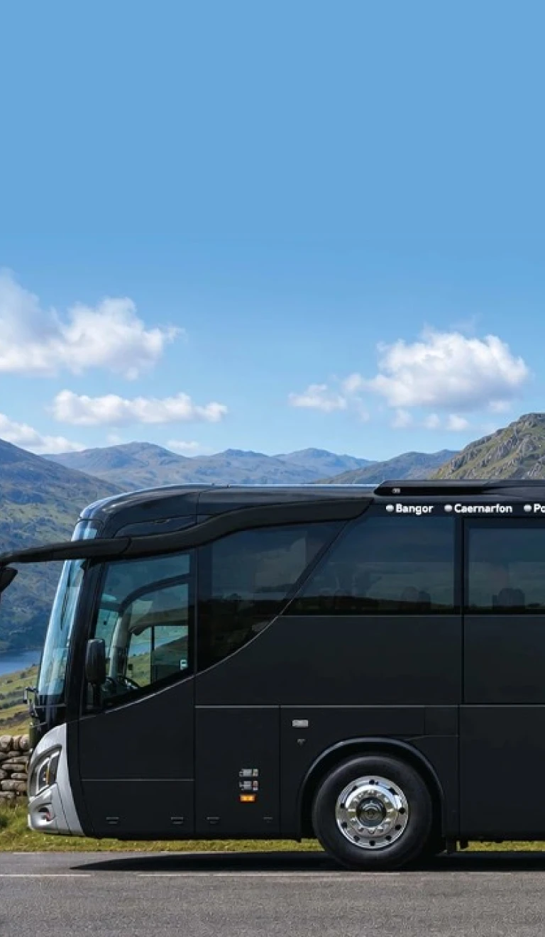 A coach parked up with views of mountains and a lake beyond.